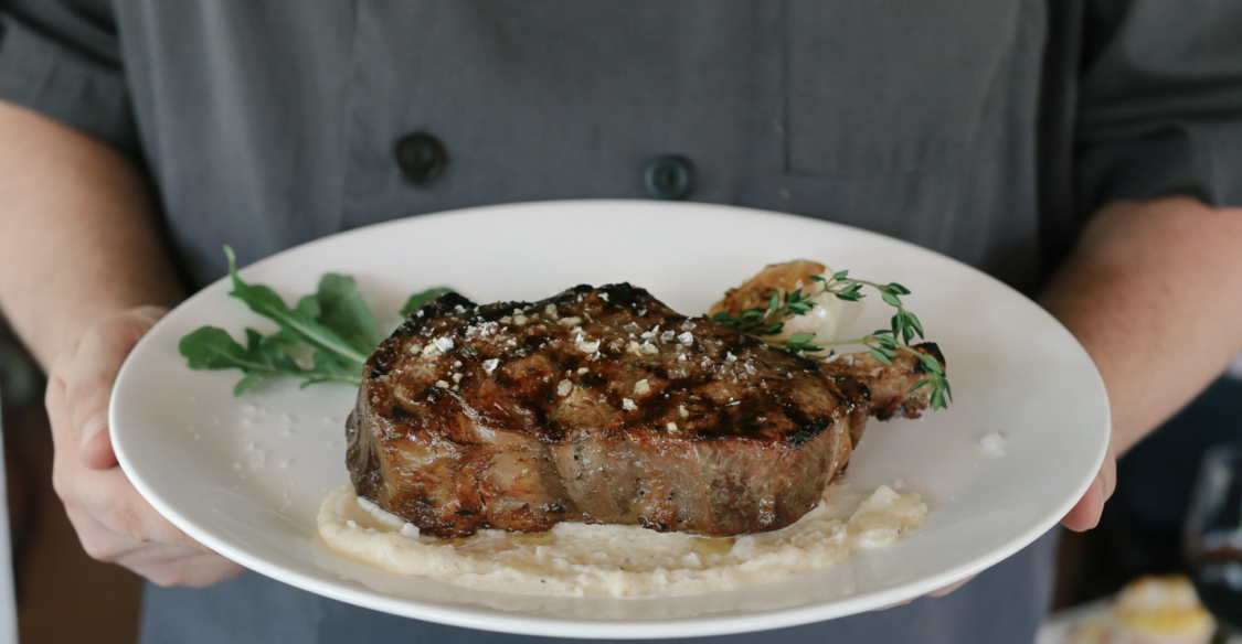 Man holding New York Strip steak on plate